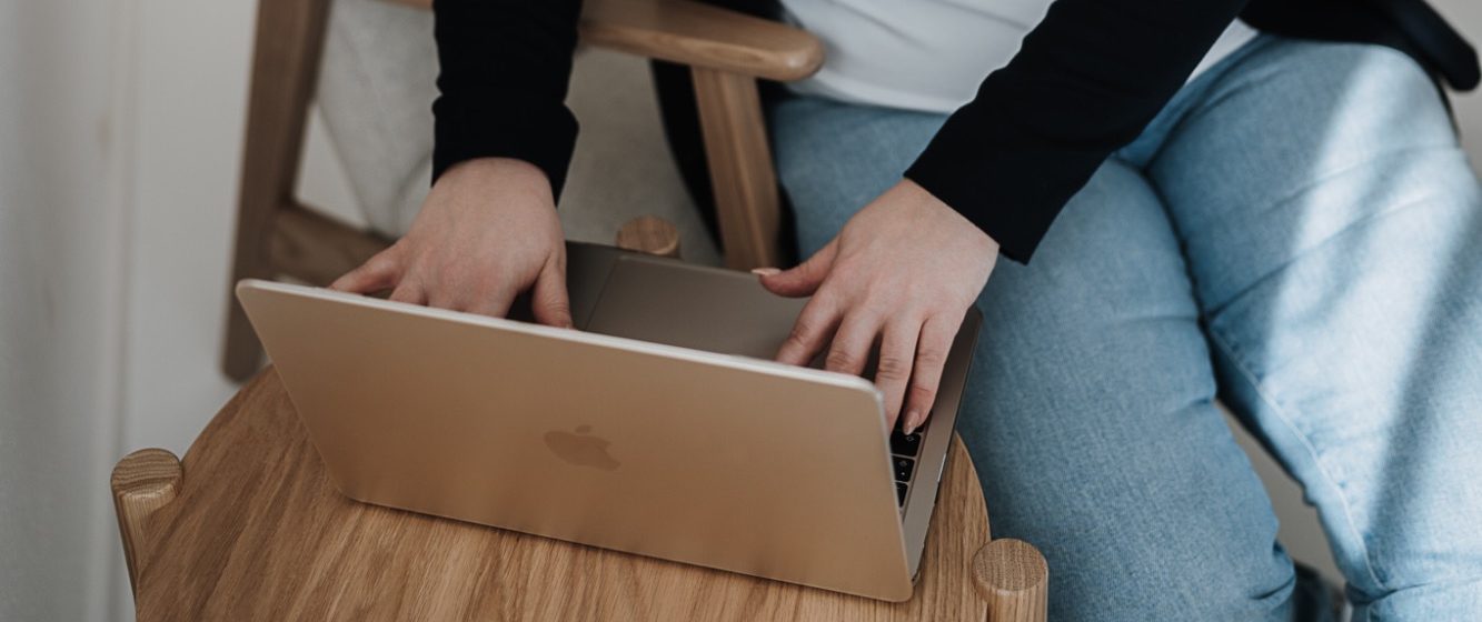 Eine Hand schreibt in ein Notizbuch, neben einer Vase mit Rosen und einem Laptop.