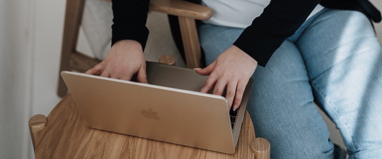 Eine Hand schreibt in ein Notizbuch, neben einer Vase mit Rosen und einem Laptop.
